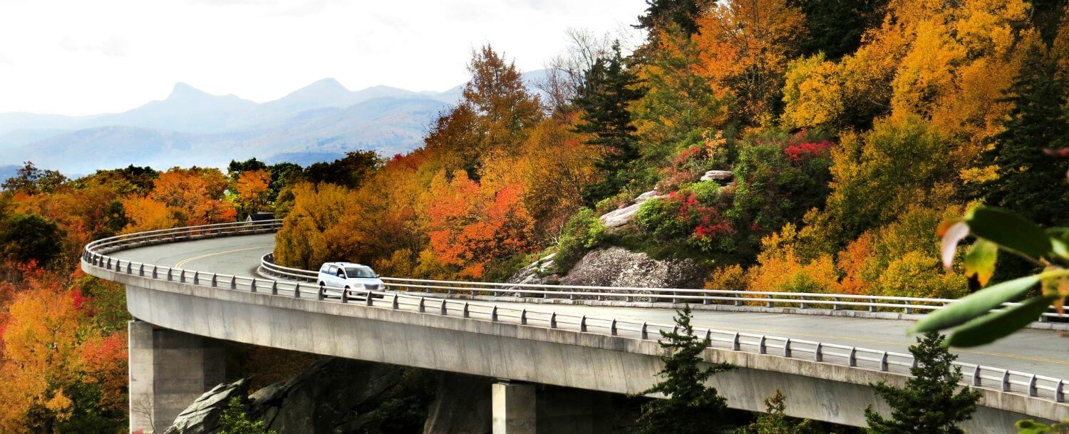 A car driving on the Blue Ridge Parkway pas a scenic mountain overlook.