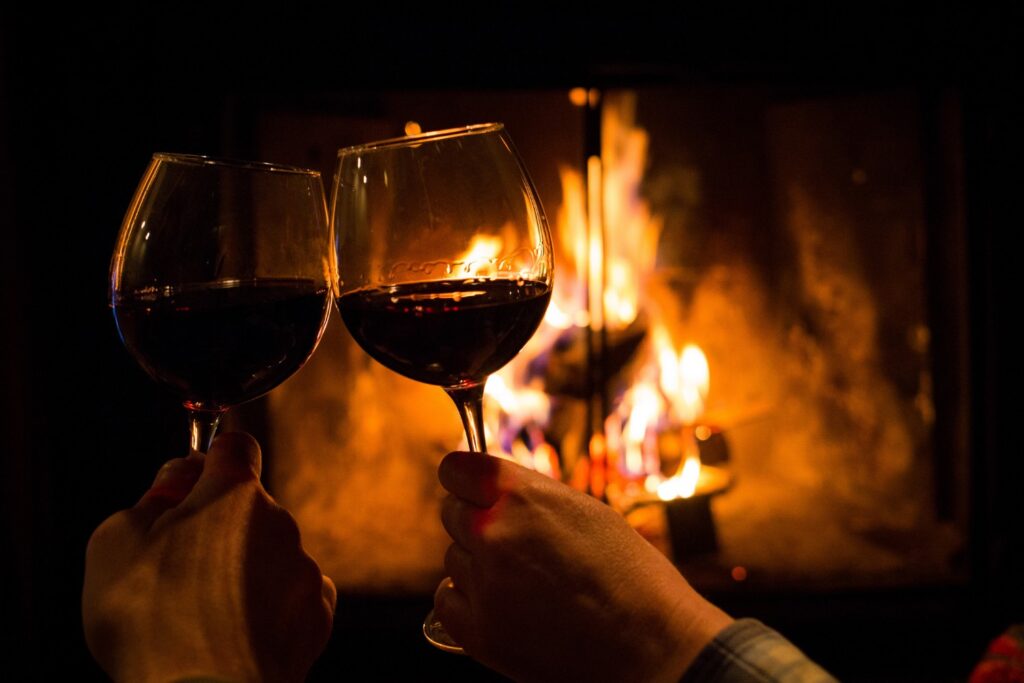 a couple holding two glasses of wine by the fireplace on a romantic getaway in NC.