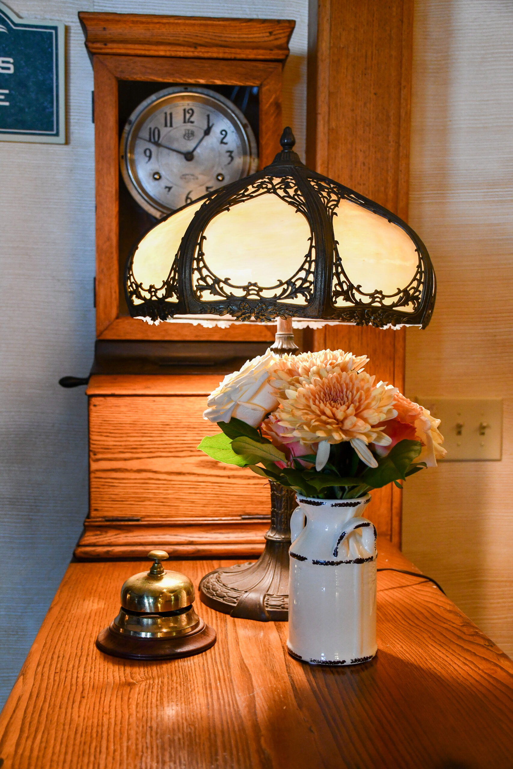 vignette of a table with a lamp, flowers, and clock in the background