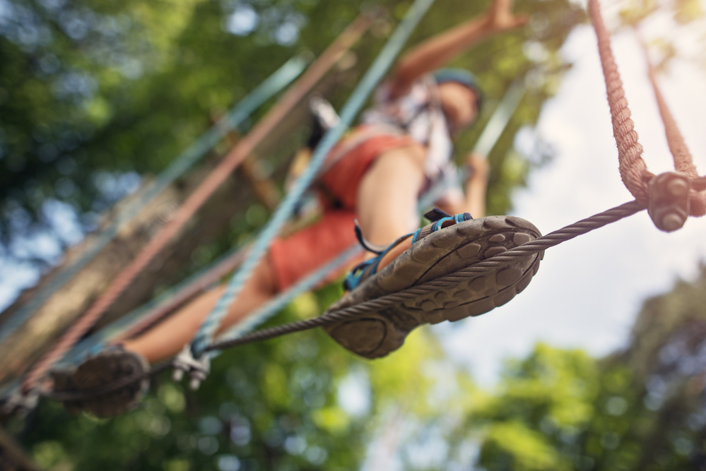 Little boy walking on line on difficult ropes course in adventure park. Sunny summer day. Focus on the line.