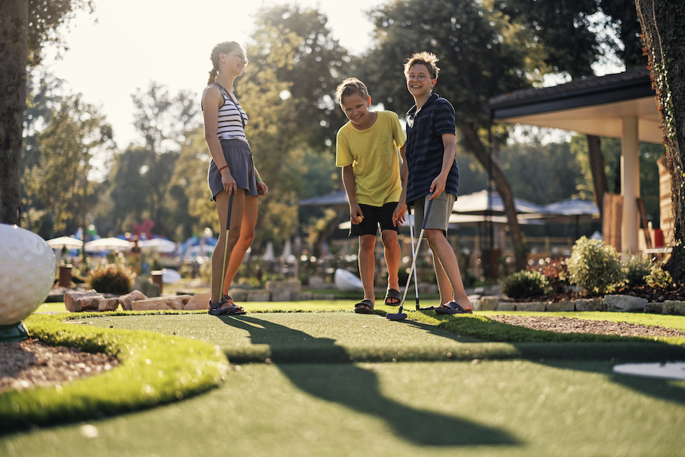 Three teenage kids having fun playing mini golf.