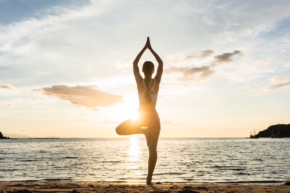 Woman doing yoga on beach at daybreak