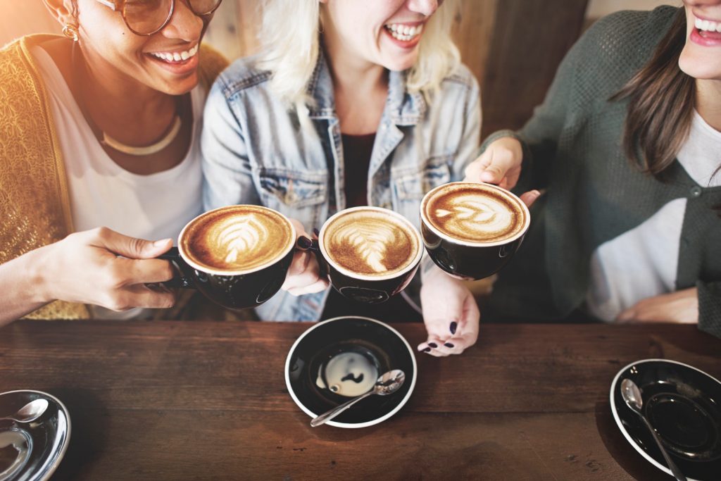 Three women chatting and holding coffee cups.