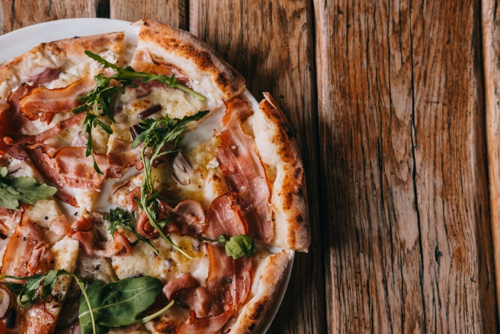Pizza with meat and arugula on wooden table