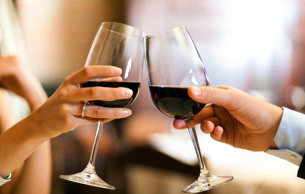 Woman and man raising a toast of glasses with red wine.