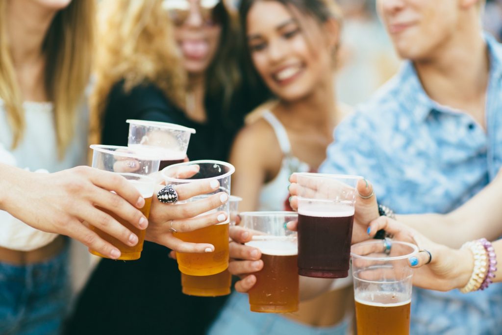 People clicking beer cups together at an outdoor beer festival.