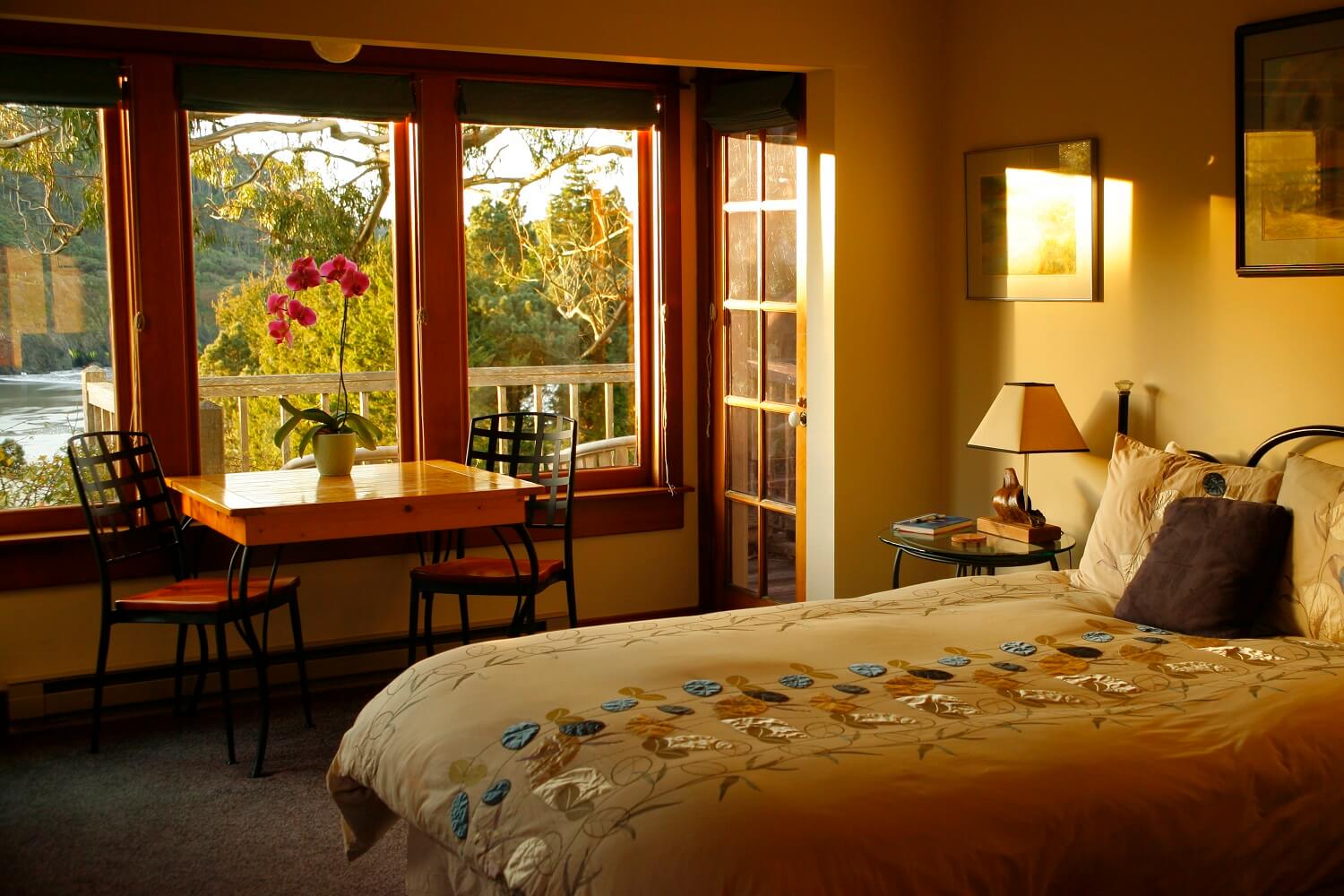Pacific Room - Bed, nightstand, table with chairs, three windows behind them, door