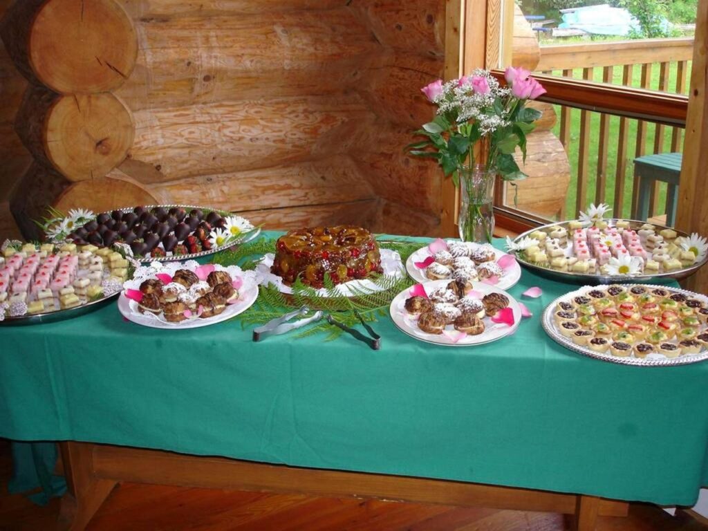 A table featuring platters of various desserts, pastries, and cakes is set up in the dining room of the lodge