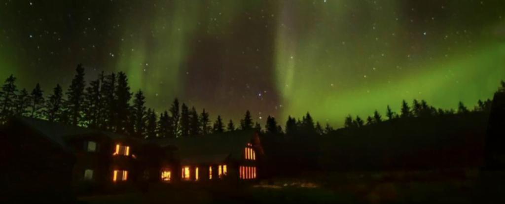 The sky is lit green with the northern lights above the lodge