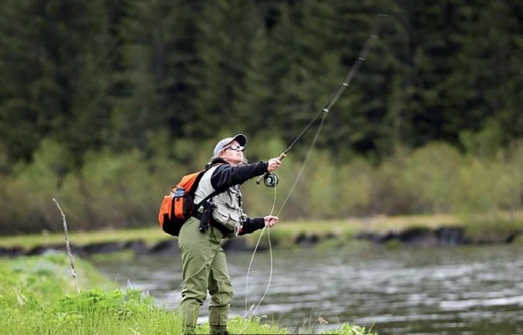Action shot of a woman fly fishing at the edge of a stream