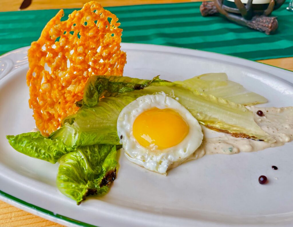 Two romaine lettuce leaves with a fried egg on top and a parmesan crisp on a bed of ceaser dressing