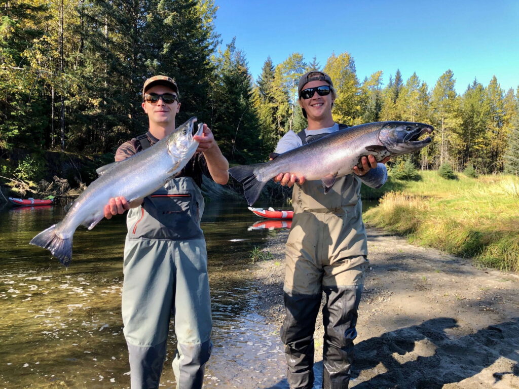 Two young men standing side by side each holding a large salmon