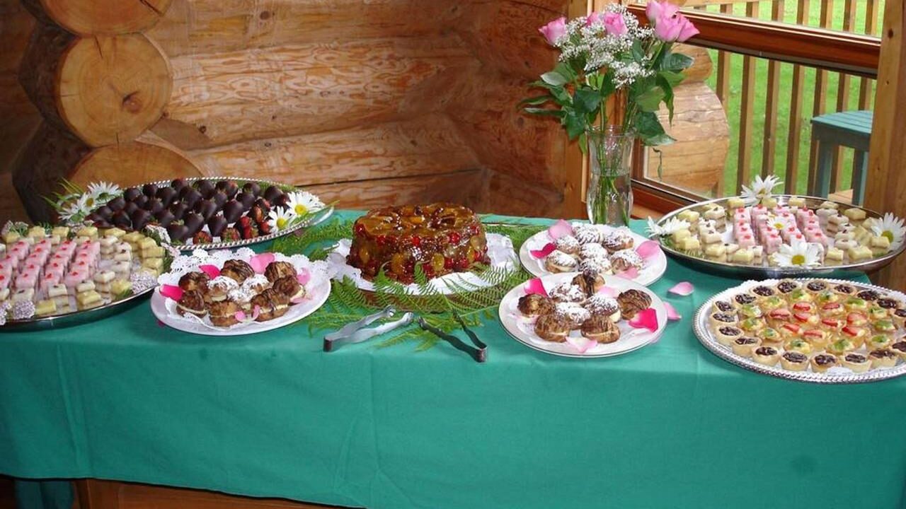 A table featuring platters of various desserts, pastries, and cakes is set up in the dining room of the lodge