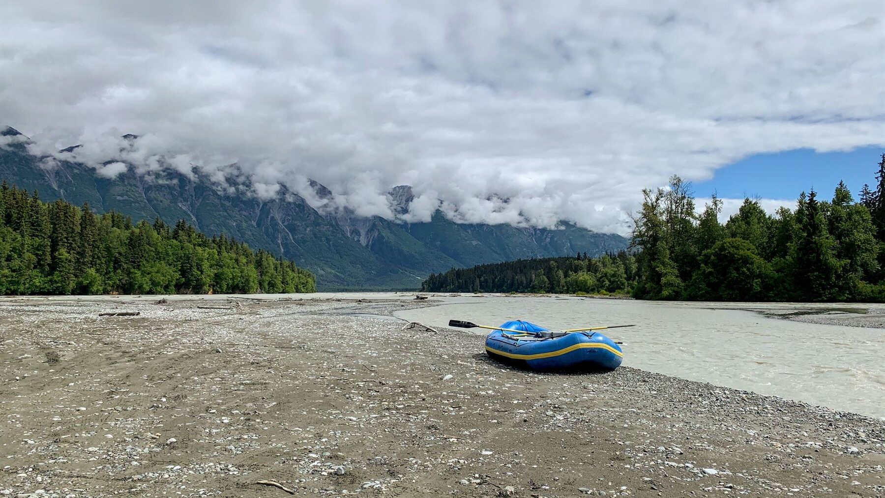 Dingy sitting beside a riverbed with forests and mountains in the distance