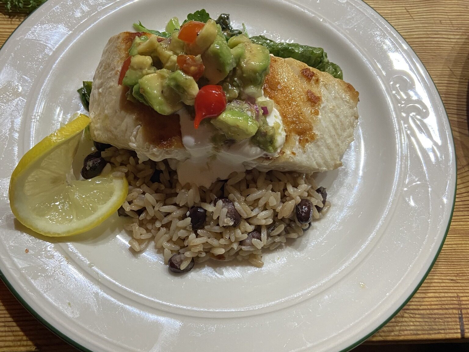 seared halibut topped with avocado on a bed of rice and beans with a lemon garnish