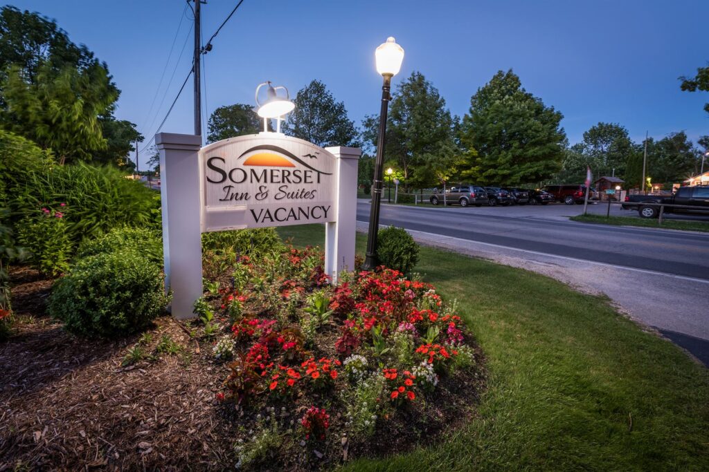 Somerset Inn & Suites sign at dusk lit up with red flowers surrounding it