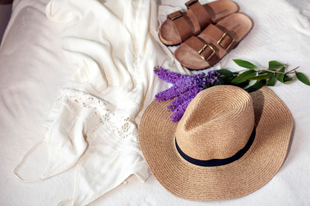 Beach hat, shoes, and lavendar plant on white linens.