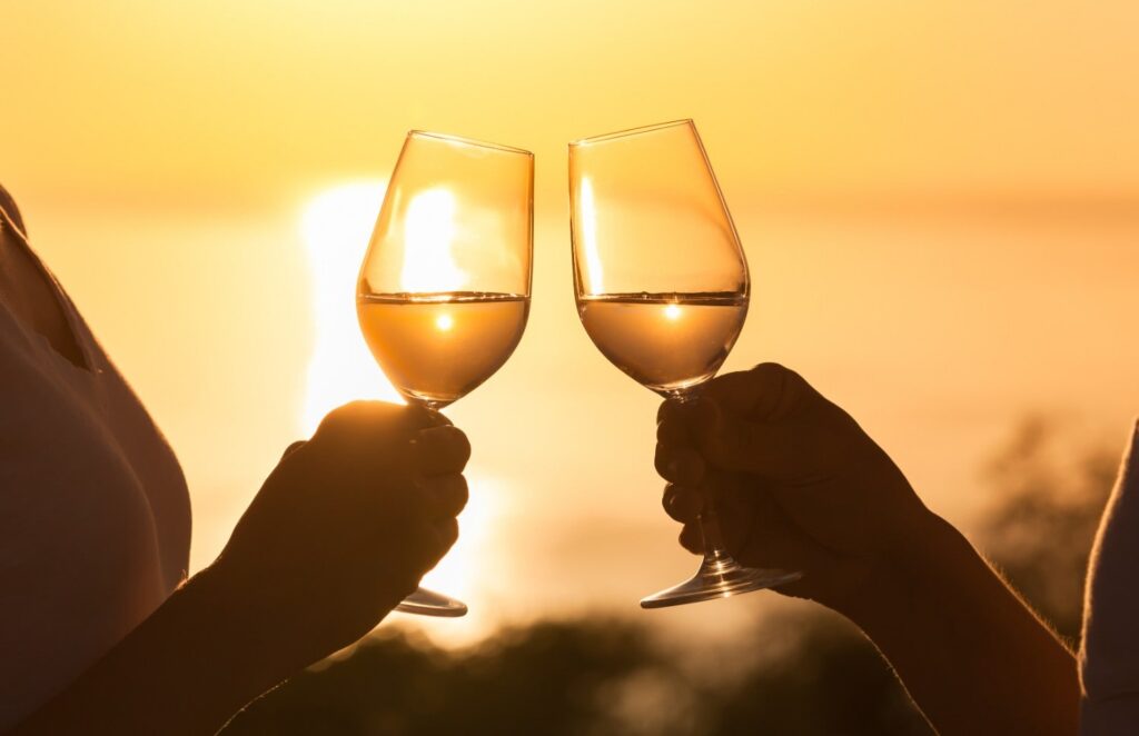 Couple toasting glasses together with sunset in the background.