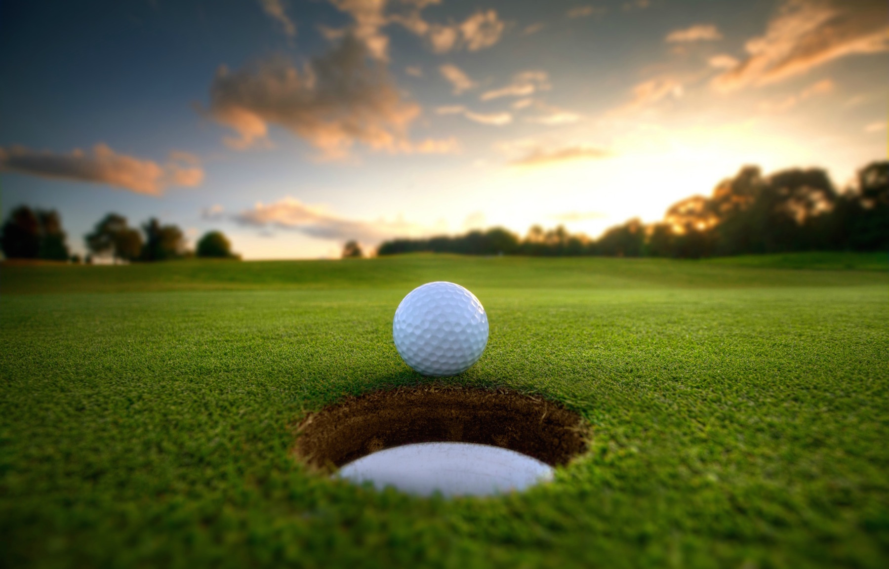 Golf ball near hole at sunset
