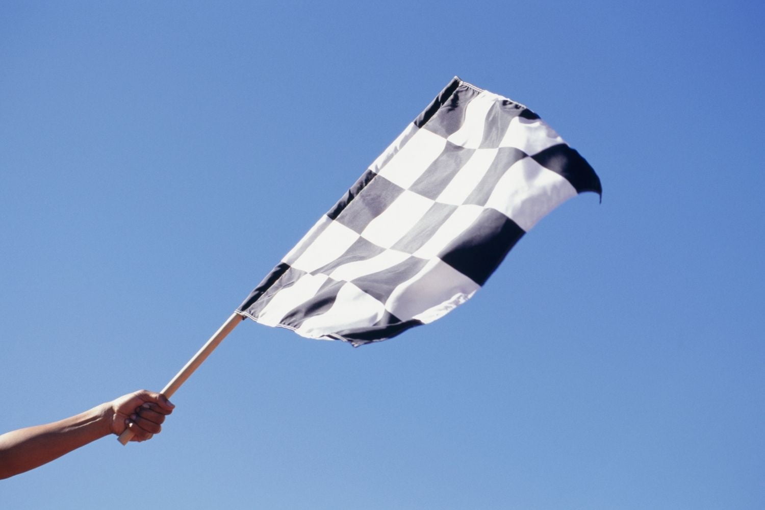 Person holding checkered flag with a blue sky background.