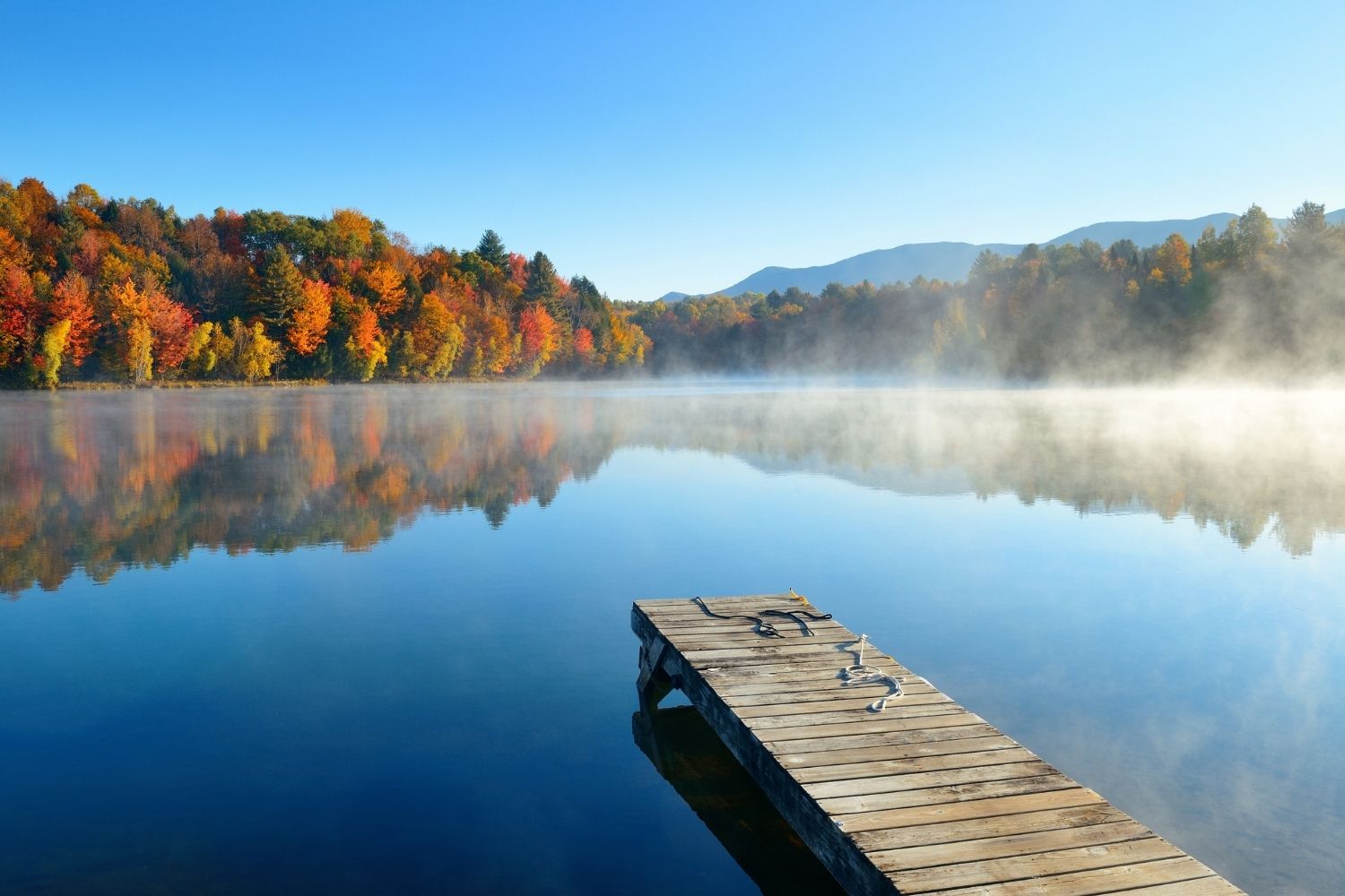 Dock on a lake with fall foliage around.