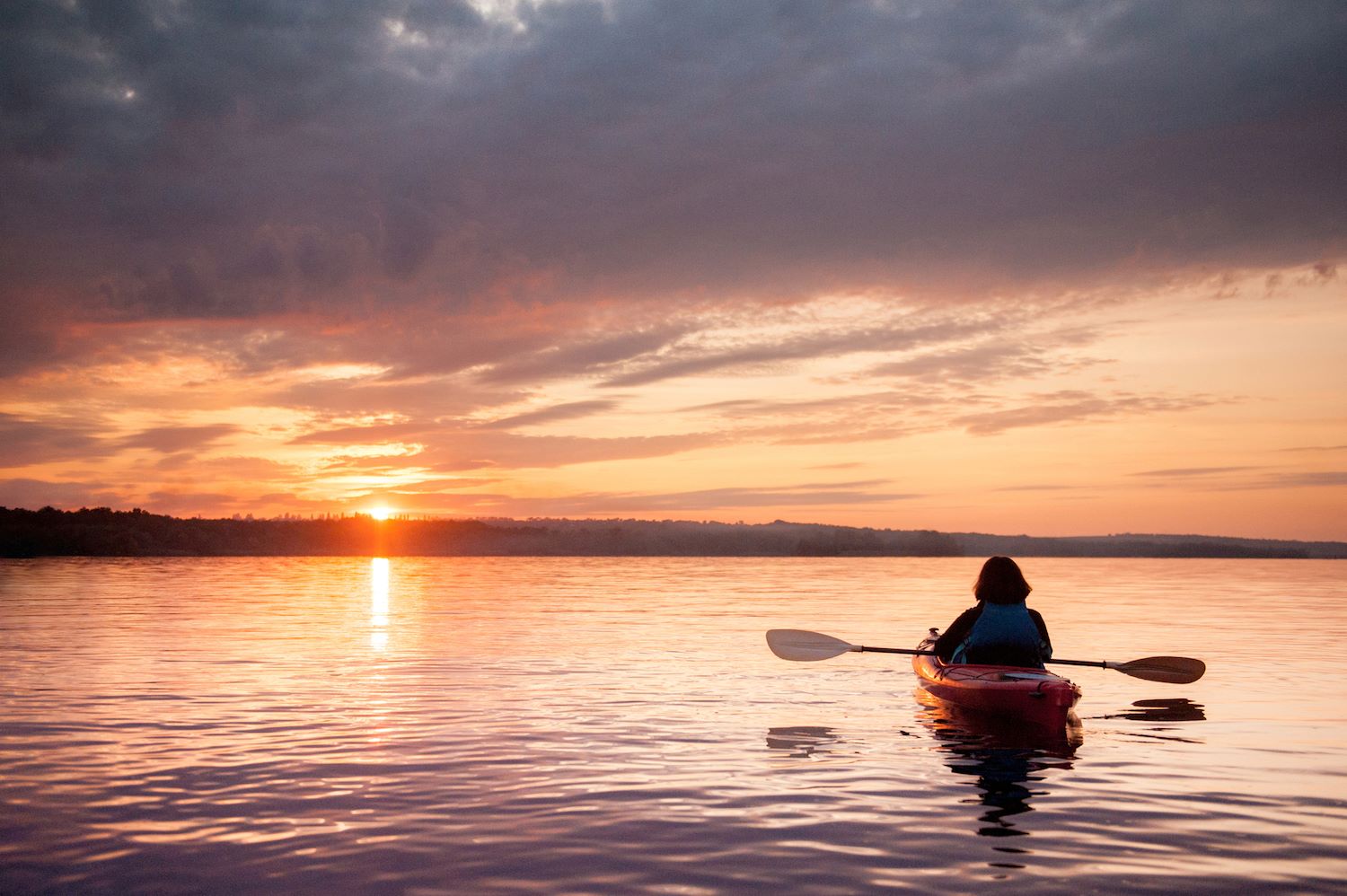 Person kayaking on a lake at sunset.
