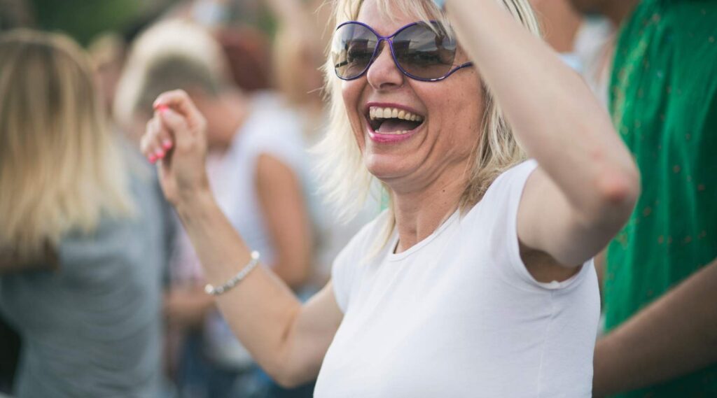 Older white woman smiling and dancing to live music outdoors