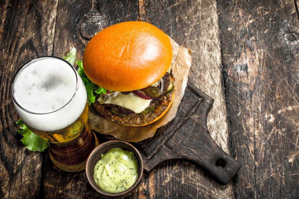 Burger and pint of beer sitting on a serving board on a wood background.
