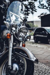 Up close photo of the front of a parked motorcycle. The background is suburban looking with a parked car.