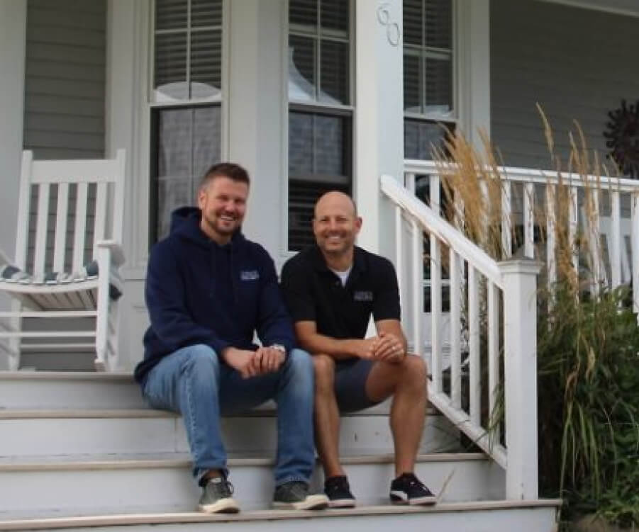 Two men smiling on porch stairs.