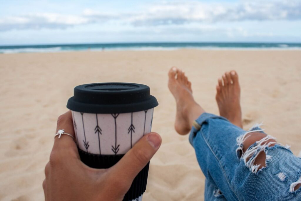 Woman sitting on the beach holding coffee.