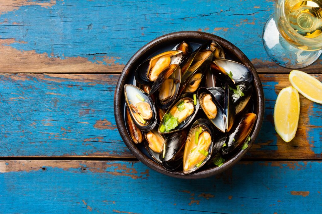 Mussels in clay bowl, glass of white wine and lemon on wooden blue background at Kiawah Island restaurant