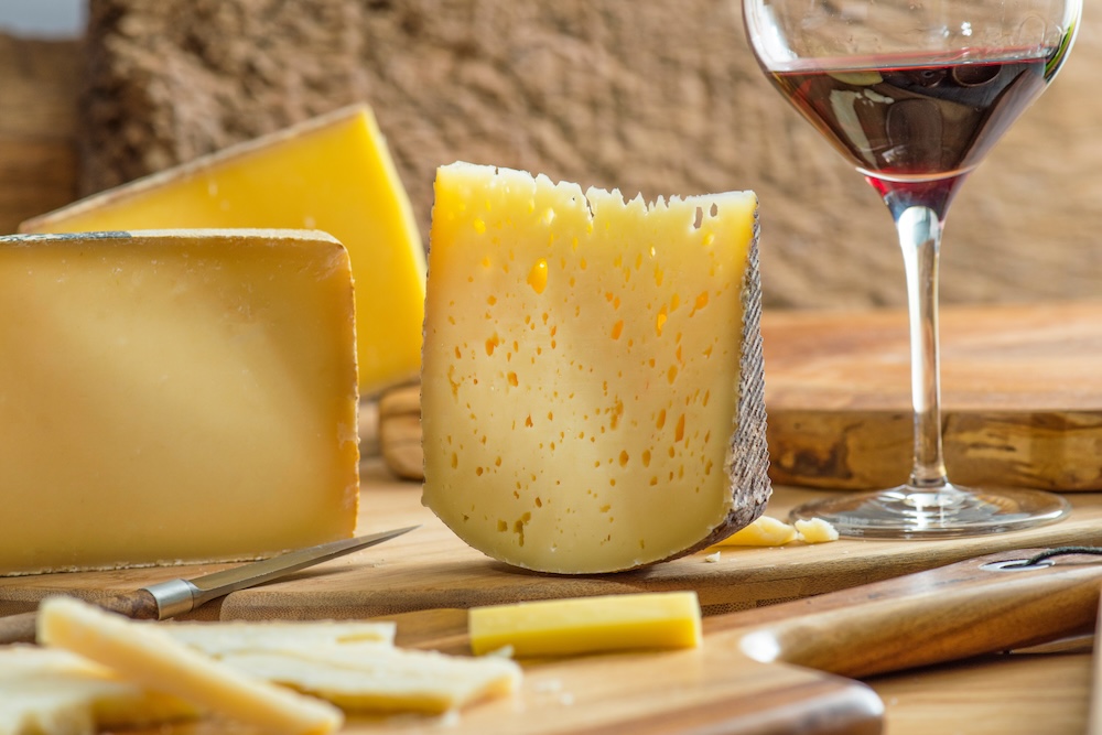 A glass of red wine sitting on a wooden cutting board with three blocks of artisan cheese