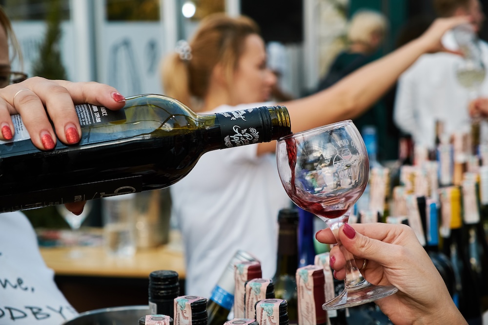A woman pouring a red wine sample into another woman's wine glass