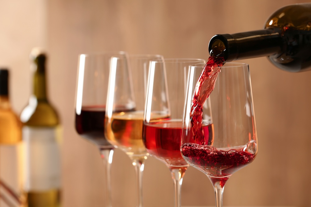 Wine being poured from a bottle into a wine glass, with three additional wine glasses in the background