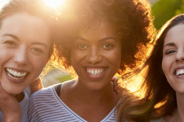 Three women smiling with sun in background