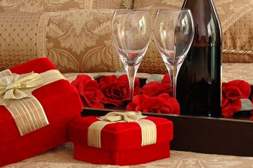 Presents wrapped in red wrapping paper with champagne glasses and roses in background