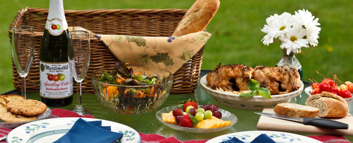 Various food set-out on table with picnic basket in background