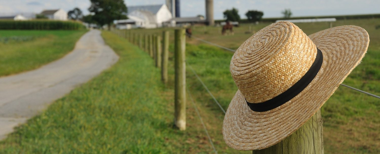 Straw hat sitting on fence post with farm land in background