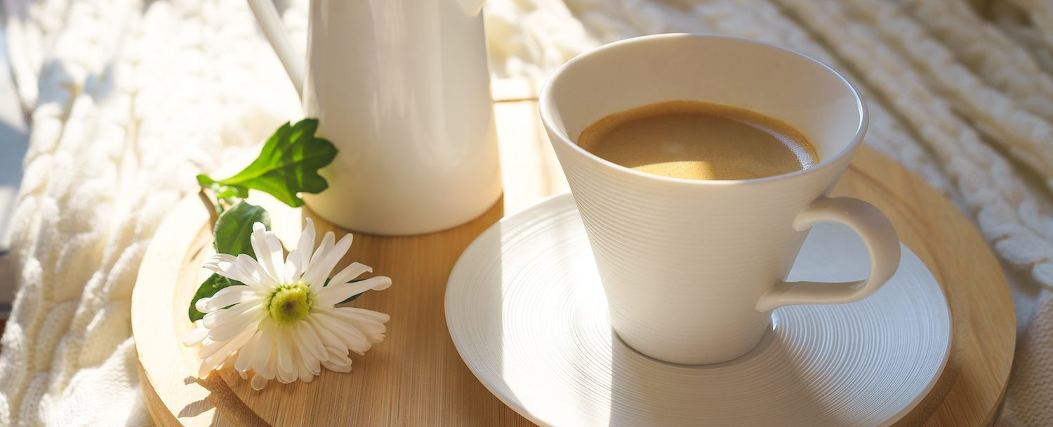Coffee cup filled with coffee sitting on tray with flower next to it.