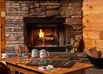 Log cabin fireplace with hot chocolate and board game in front of it.