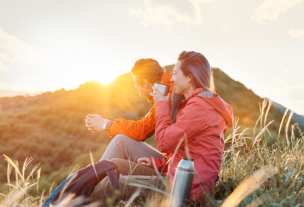 Couple sitting at the summit of a mountain at sunset.