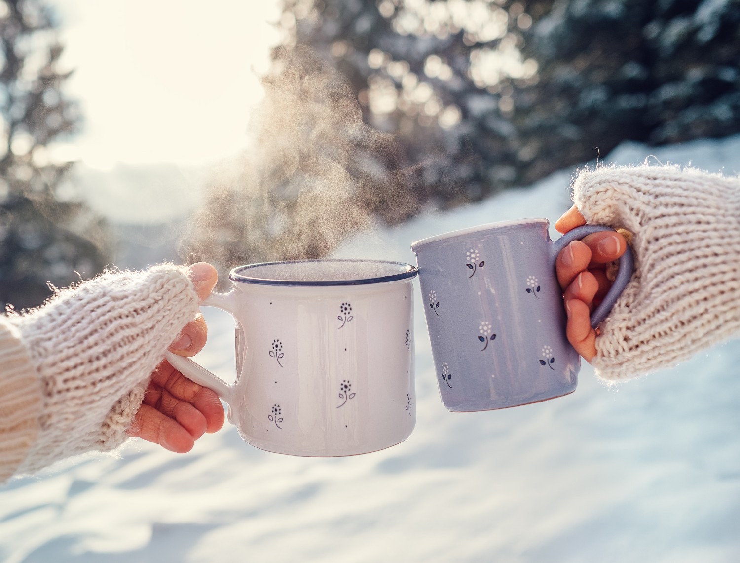 Man and woman hands in knitting mittens with cups of hot tea on winter forest glade