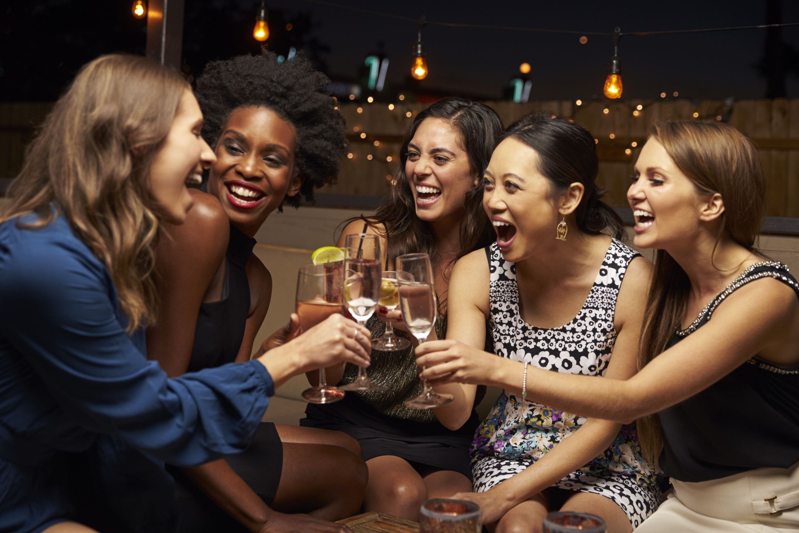 5 women toasting drinks and smiling at a party