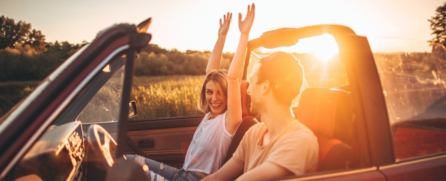 Woman hold hands up as man drive convertible both smiling