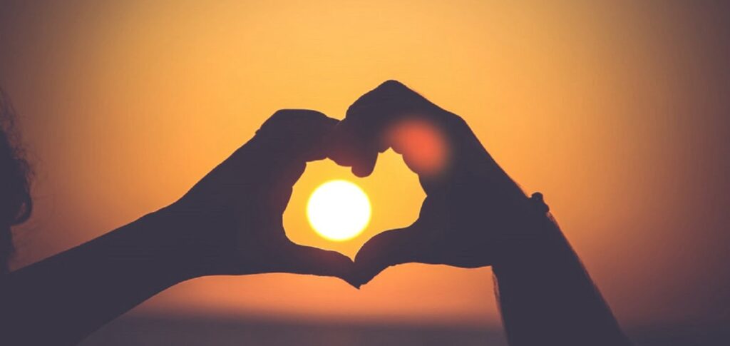 Hands making a heart around a sunset