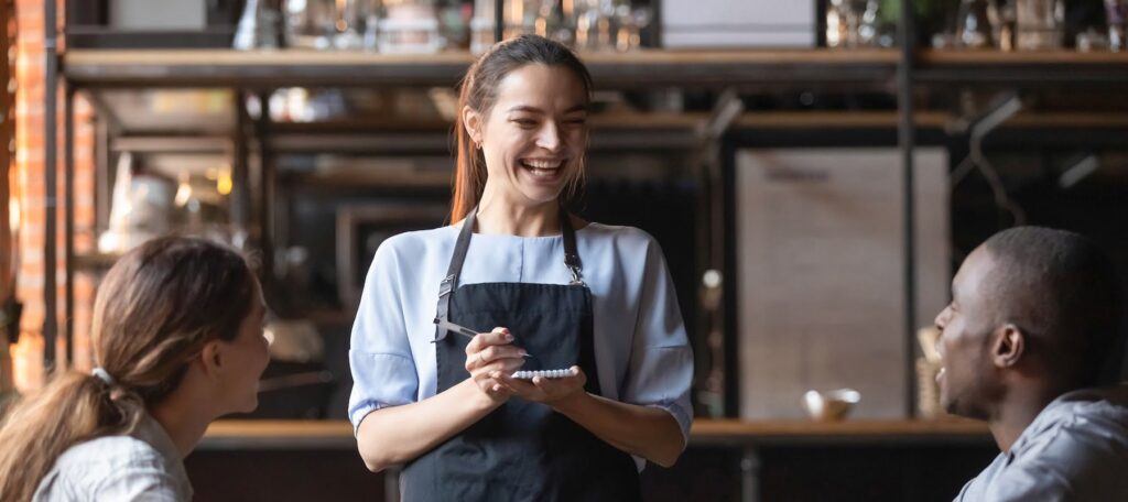 Attractive waitress laughing at African American man funny joke, serving customers, diverse couple making order in cafe, coffeehouse female worker and multiracial visitors having fun (Attractive waitress laughing at African American man funny joke, se