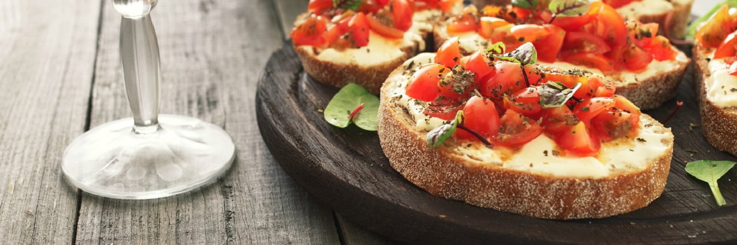 Bruschetta with tomatoes goat cheese and basil on a wooden table with a glass of wine. Tasty appetizer for wine.