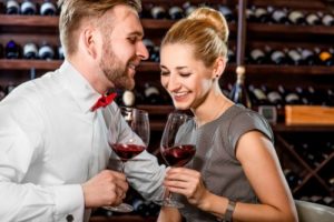 Young well-dressed couple smiling and having romantic wine tasting at the cellar
