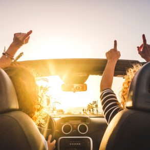 Two ladies with hands up driving with sun up